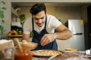 Professional Italian chef baking a cheesy Hawaiian pizza at home. Italian chef topping a Hawaiian pizza with mozzarella cheese, tomato sauce, vegetable, and meat before bake in the oven.