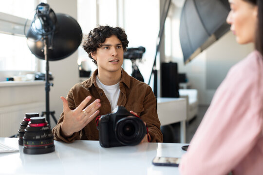 Male photographer talking with model about the reference images that customers need, preparing for photoshoot in studio