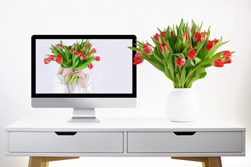 a mono block computer and a vase with spring tulips stand on a white table in a Scandinavian style