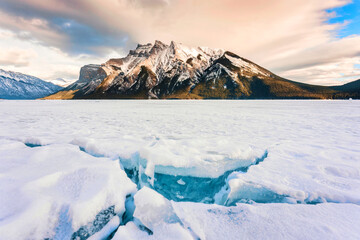Frozen Lake Minnewanka with rocky mountains and cracked ice from the lake in winter at Banff national park - obrazy, fototapety, plakaty