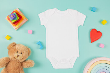 White cotton baby short sleeve bodysuit, teddy bear and natural wooden eco-friendly toys on pastel background. Infant onesie mockup. Blank gender neutral newborn bodysuit template mock up. Top view - obrazy, fototapety, plakaty