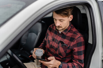 man hold cup with coffee use mobile phone sit in the car take a brake