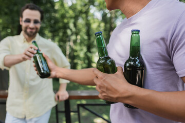 african american man giving fresh beer to blurred friend in park.