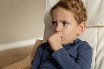 A little boy sits with a tense face and sucks the thumb of his left hand.