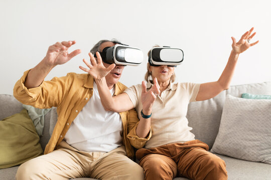 Senior couple having fun with virtual reality glasses, sitting on sofa and gesturing - Powered by Adobe