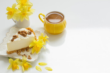 cheesecake with cup of tea and yellow spring flowers on white table
