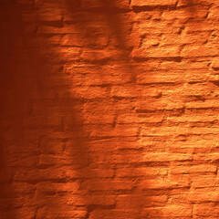 Orange red brown brick wall of the house. Close-up. Sunlight and shade from tree leaves. Bright vintage background for design. Burnt orange color shade. Rough surface texture. Painted plaster.