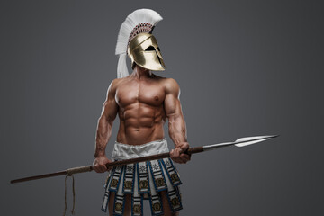 Studio shot of strong greek man with plumed helmet and spear against gray background.