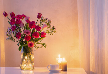 pink flowers in glass modern vase with burning candles in white interior