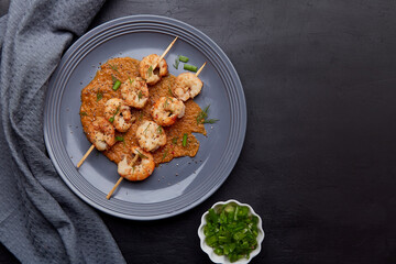 Grilled shrimps on skewers on the plate with coy space. Seafood barbecue, roast prawns flat lay. Party snacks.