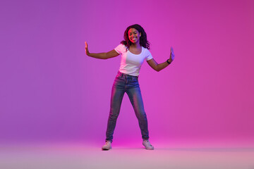 Fototapeta na wymiar Joyful African American Female Dancing In Neon Light Over Purple Background