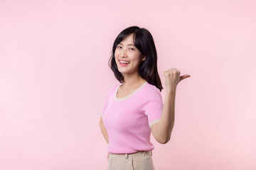 Portrait young beautiful asian woman happy smile pointing finger and hand to showing on copy space isolated on pink background. Attractive female person gesture attention to this promotion.