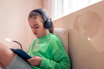 Little girl in headphones with a tablet in her room.