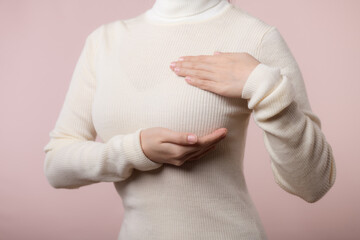 Woman hands checking lumps on her breast for signs of breast cancer on pink background. Healthcare...