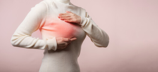 Woman hands checking lumps on her breast for signs of breast cancer on pink background. Healthcare...