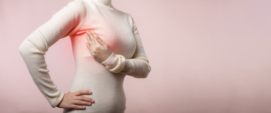 Woman hands checking lumps on her breast for signs of breast cancer on pink background. Healthcare world health day concept.