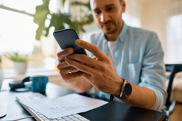 Close up of entrepreneur using smart phone while working at home.