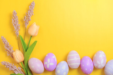 Happy Easter holiday greeting card design concept. Colorful Easter Eggs and spring flowers on yellow background. Flat lay, top view, copy space.
