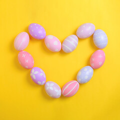 Happy easter holiday celebration concept. Group of painted colourful eggs in heart shape decoration on a yellow background. Seasonal religion tradition design. Top view, flat lay, copy space.