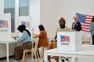 Selective focus on desk with ballot box for papers with candidates chosen by voters on background...