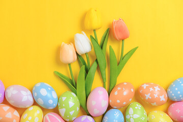 Obraz na płótnie Canvas Happy Easter holiday greeting card design concept. Colorful Easter Eggs and spring flowers on yellow background. Flat lay, top view, copy space.
