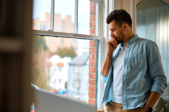 Distraught man looking through window at home.