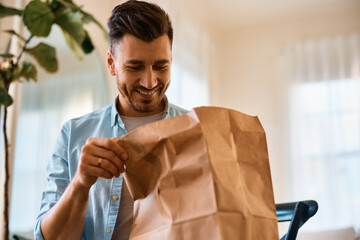 Happy man looking at food in delivery paper bag at home.