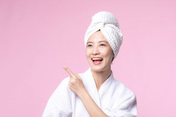 Beautiful young asian woman happy smile face with hand or finger gesture signs in bathrobe and shower towel showing empty space isolated on pink background.