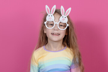 Cute little child girl wearing bunny ears glasses a on Easter day. Easter girl portrait on pink background, funny emotions, surprise.