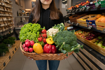 a young girl with a wooden basket full of fresh vegetables in her hands stands in a store