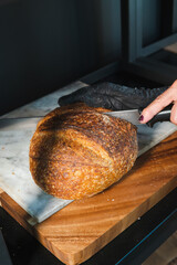 freshly baked bread on a wooden board on a sunny morning is cut with a knife