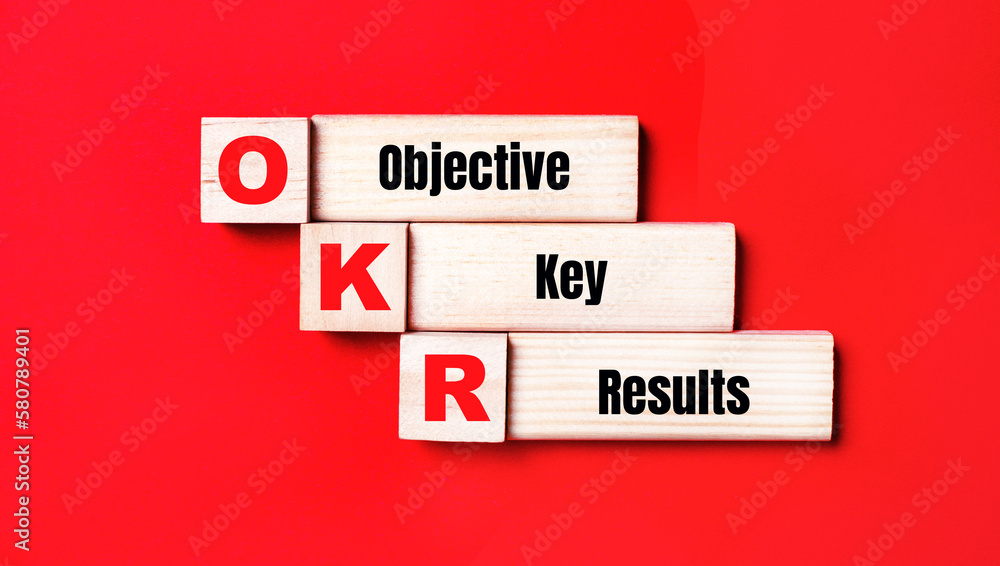 Poster on a bright red background, wooden cubes and blocks with the text okr objective key results. manufac