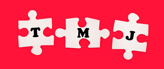 Three white jigsaw puzzles with the text TMJ on a bright red background.