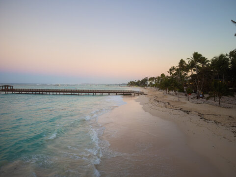 Sandy beach and sea. Lots of palm trees on the beach. Wooden bridge, pier. Twilight. Resort place, romance, solitude, vacation.