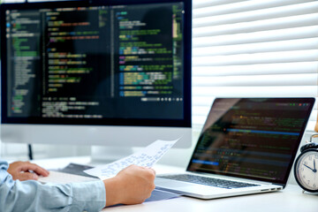 programmer writing program code with two monitors and working on a new software or hacker...