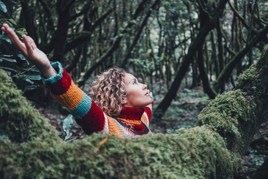 Woman celebrating nature lifestyle and outdoor leisure activity alone opening arms outstretching and looking the trees in forest green woods outdoor. Inner life balance mindful lifestyle female people