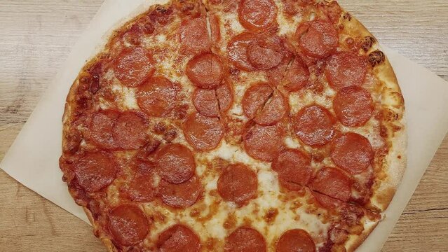Top view shot of delicious pepperoni pizza with mozzarella cheese on wooden table in the kitchen.