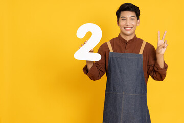 Restaurant owner sme young Asian man holding number 2 or two isolated on yellow background