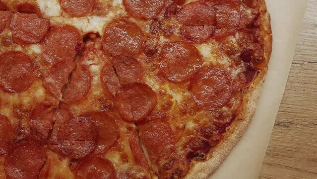 Top view shot of delicious pepperoni pizza with mozzarella cheese on wooden table in the kitchen.