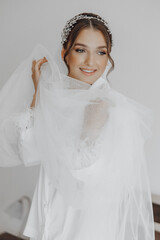 Morning of bride before the wedding. Beautiful young woman with long veil in a white robe. Natural beauty and professional make-up.Girl in white lace boudoir dress.