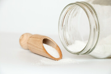 Edible salt in a wooden spoon and a glass jar next to it on a white background