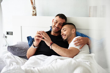 Male couple smiling while enjoying time together in the bed at home.