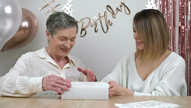 Elderly mother celebrates her birthday. A loving and caring adult daughter gives her mother a box with a gift. Family values.