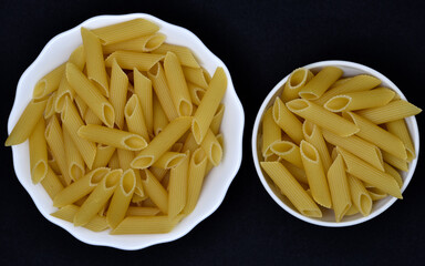 Wheat pasta in a white bowl on a black background. Dry pasta.