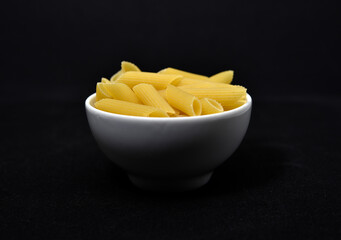 Wheat pasta in a white bowl on a black background. Dry pasta.