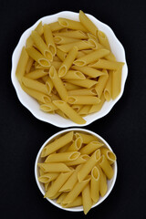 Wheat pasta in a white bowl on a black background. Dry pasta.