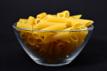 Wheat pasta in a glass bowl on a black background. Dry pasta in a transparent container.