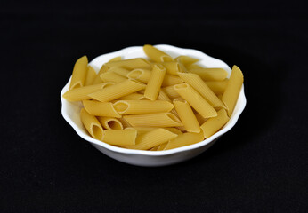 Wheat pasta in a white bowl on a black background. Dry pasta.