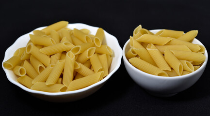 Wheat pasta in a white bowl on a black background. Dry pasta.
