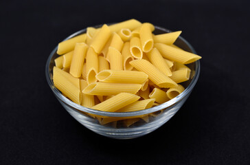 Wheat pasta in a glass bowl on a black background. Dry pasta in a transparent container.